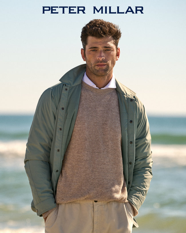 Man at the beach wearing a beige sweater and matching pants by Peter Millar, layered with a green jacket