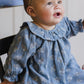 A baby wearing the Quincy Mae Baby Girls' and Girls' Long Sleeve Isla Dress sits on a chair, gazing upward with an open-mouthed expression.