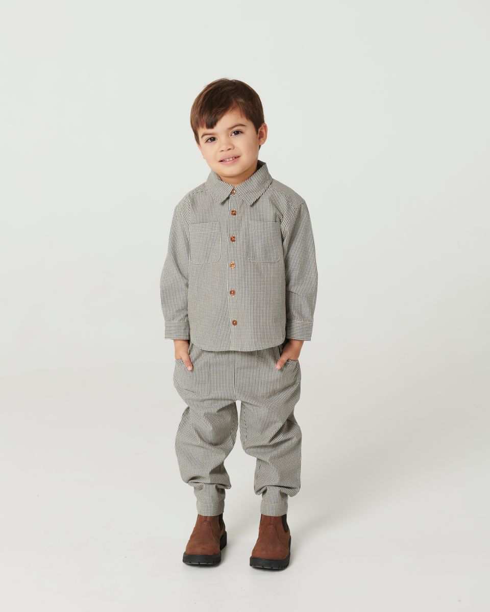 A young child faces forward in the Baby Boys’ and Boys’ Checkered Classic Shirt by Copenhagen Colors, paired with pants and brown boots, against a plain white background.