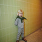 A young child with blonde hair wears the Baby Boys’ and Boys’ Checkered Classic Shirt by Copenhagen Colors under a light-grey suit, with a green sweater and brown boots.