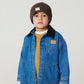 A young child wears the Copenhagen Colors Boys’ Denim Jacket with Corduroy Collar, a brown knit beanie, mustard sweater, and light brown pants against a plain background.