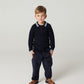 Young child on a plain background wears the Copenhagen Colors Boys’ Knitted Waffle Polo Long-Sleeved Polo, dark pants, and brown shoes, standing with hands by their sides.