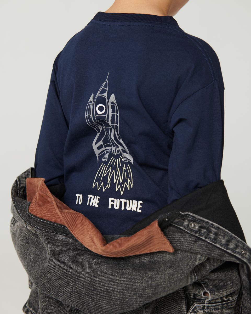 A child wears the Copenhagen Colors Boys’ To the Future Long Sleeve T-Shirt (navy, rocket graphic, “TO THE FUTURE” on back), holding a gray jacket for comfort.