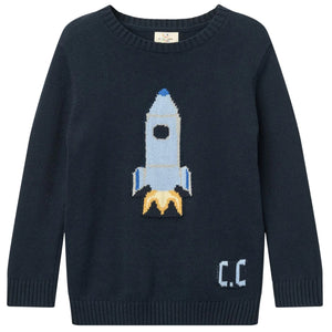 The Copenhagen Colors Baby Boys’ and Boys’ Rocket Sweater is navy blue, featuring a blue and white rocket with yellow flames and “C.C.” on the lower right side.