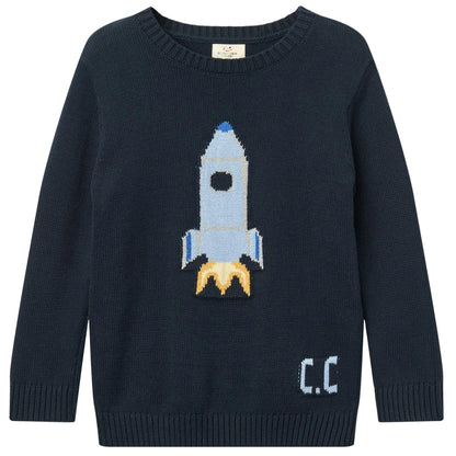 The Copenhagen Colors Baby Boys’ and Boys’ Rocket Sweater is navy blue, featuring a blue and white rocket with yellow flames and “C.C.” on the lower right side.