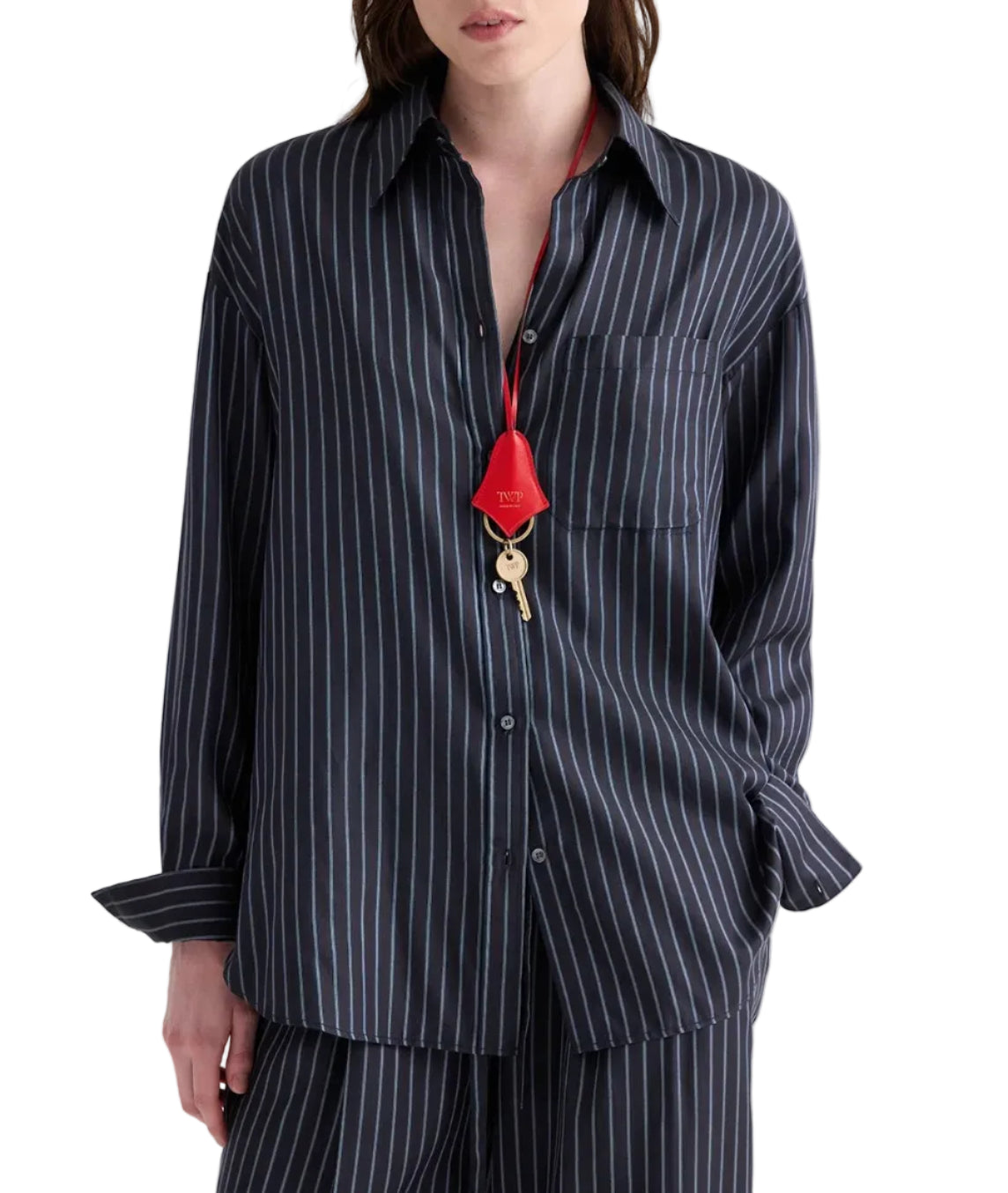 A person wearing the TWP Big Joe Evening Stripe Silk Shirt—an elegant, dark, menswear-inspired pinstriped button-up—paired with matching pants and accessorized with a red lanyard and key around their neck.