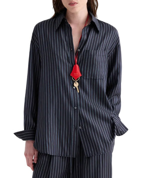 A person wearing the TWP Big Joe Evening Stripe Silk Shirt—an elegant, dark, menswear-inspired pinstriped button-up—paired with matching pants and accessorized with a red lanyard and key around their neck.