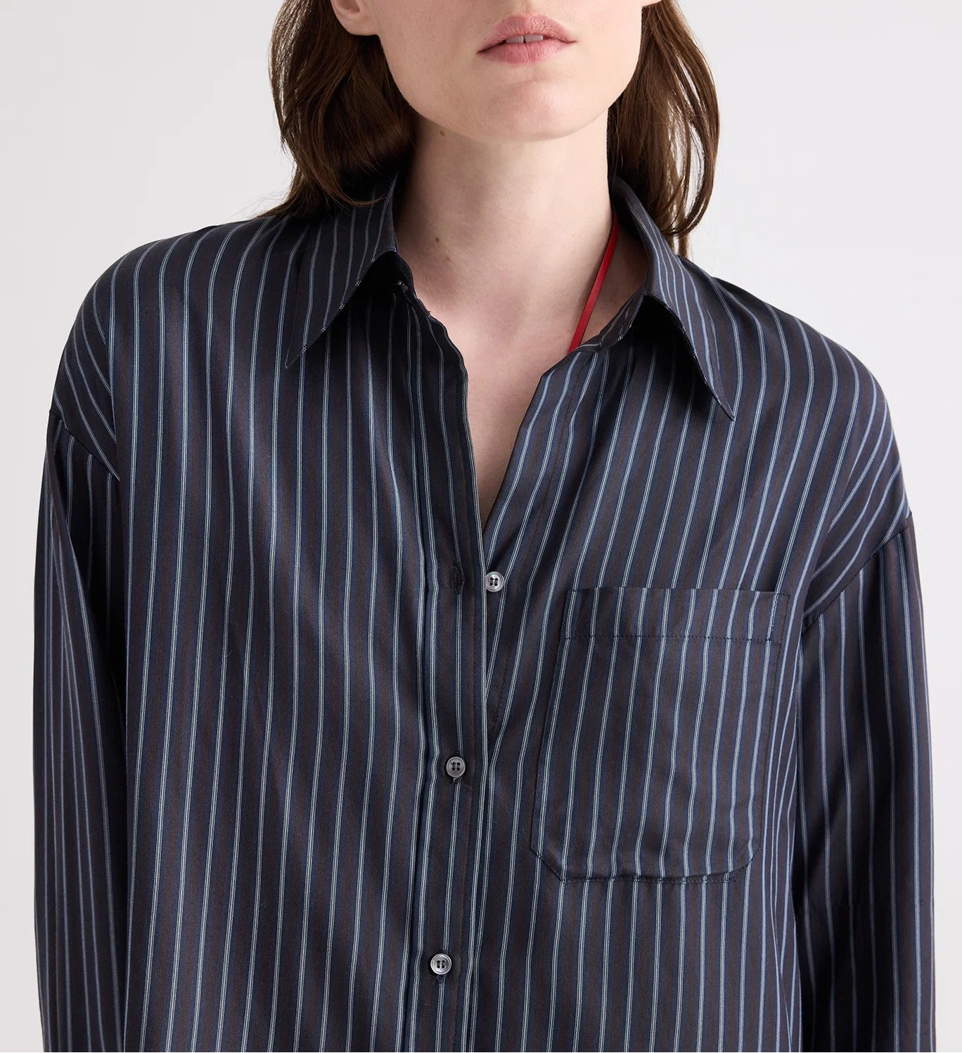A person wearing the TWP Big Joe Evening Stripe Silk Shirt—a menswear-inspired black button-up featuring blue vertical stripes and a front chest pocket—shown from shoulders to mid-torso.