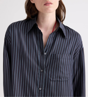 A person wearing the TWP Big Joe Evening Stripe Silk Shirt—a menswear-inspired black button-up featuring blue vertical stripes and a front chest pocket—shown from shoulders to mid-torso.