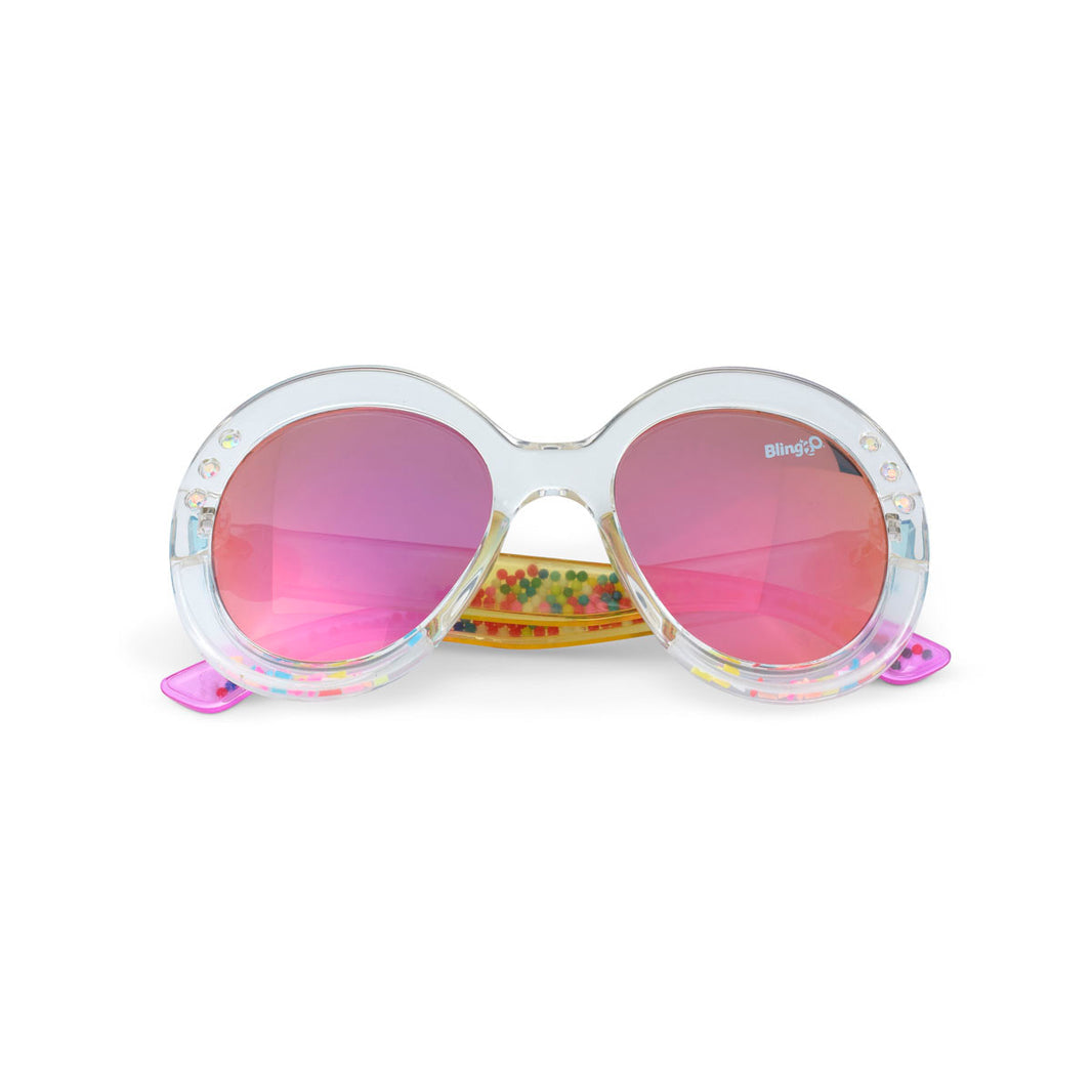 Bling2O Girls’ Glass Beach Sprinkle Sunrise Sunglasses feature child-size, round translucent frames with pink-tinted UV-protected lenses and a playful sprinkle-inspired design with colorful beads inside the frames.