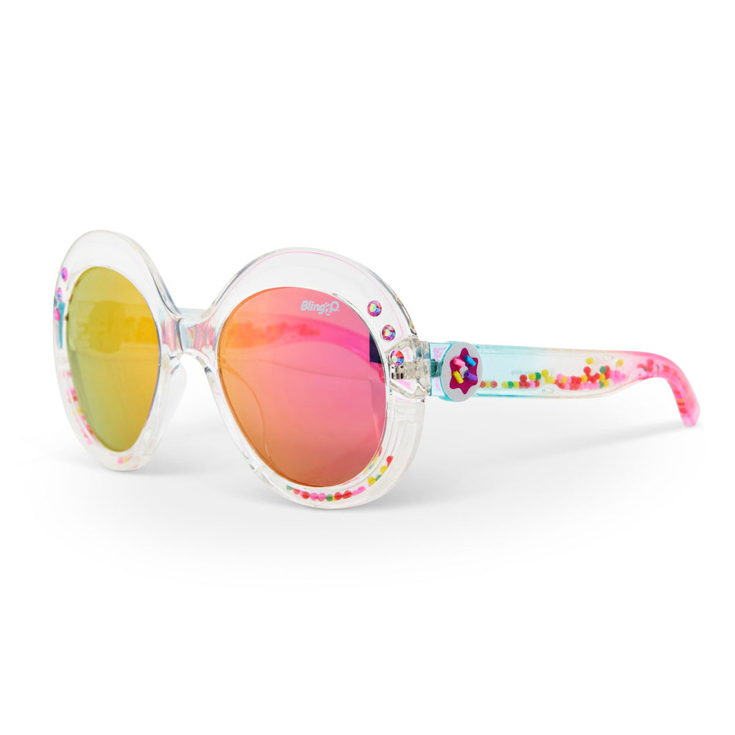 The Bling2O Girls’ Glass Beach Sprinkle Sunrise Sunglasses feature clear round frames, pink and yellow mirrored UV-protected lenses, and a fun sprinkle-inspired design with colorful beads inside the arms.