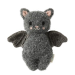 The Baby Bat - Charcoal by Cuddle + Kind is a handcrafted gray plush bat toy made from soft cotton, featuring a textured body, black wings, small ears, a smiling face, and light pink accents on the cheeks—an ideal soft companion for babies—shown against a white background.