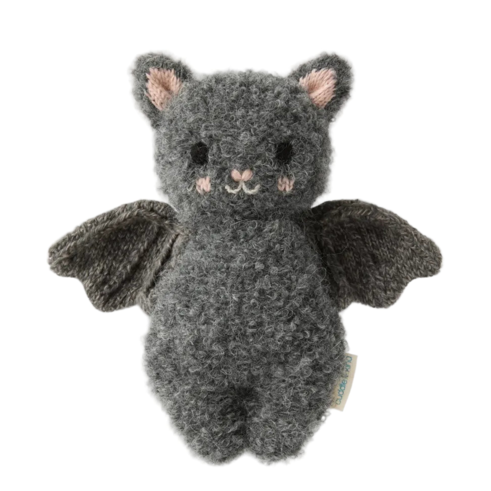 The Baby Bat - Charcoal by Cuddle + Kind is a handcrafted gray plush bat toy made from soft cotton, featuring a textured body, black wings, small ears, a smiling face, and light pink accents on the cheeks—an ideal soft companion for babies—shown against a white background.