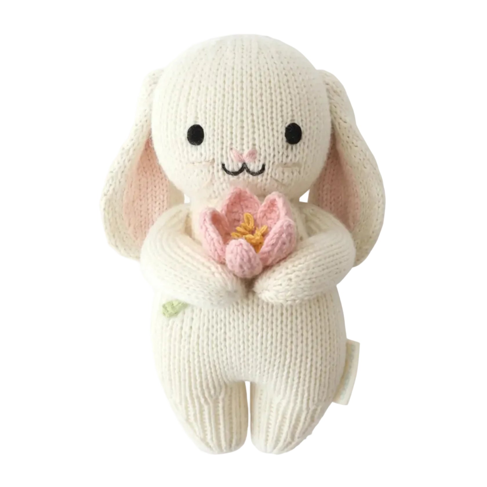 The Cuddle + Kind Baby Bunny - Blooming Tulip is an heirloom-quality, handcrafted cotton yarn plush bunny featuring black eyes, a small embroidered smile, and holding a pink tulip flower, displayed on a white background.