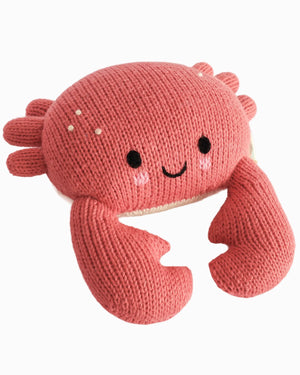 Handcrafted from soft Peruvian cotton, the Cuddle + Kind Baby Crab Coral is a knitted plush toy featuring large claws, a round pink body, black eyes, a smiling mouth, and small decorative dots—an heirloom baby animal set against a crisp white background.