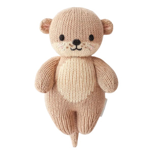 Handcrafted from heirloom-quality Peruvian cotton, the Cuddle + Kind Baby Otter is a knitted stuffed toy featuring beige and light brown yarn, black eyes, a small smile, and a cream-colored belly—making it a soft and charming companion for babies.