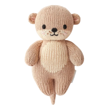 Handcrafted from heirloom-quality Peruvian cotton, the Cuddle + Kind Baby Otter is a knitted stuffed toy featuring beige and light brown yarn, black eyes, a small smile, and a cream-colored belly—making it a soft and charming companion for babies.