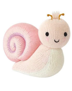 The Snail - Baby 7" from Cuddle + Kind is a hand-knit toy featuring a pink spiral shell, cream body, smiling face, and small brown antennae, crafted from soft Peruvian cotton yarn for heirloom-quality charm.