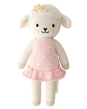 Eleanor the Lamb by Cuddle + Kind is a charming 20" knitted stuffed animal, shown against a white background, featuring a pink dress with yellow polka dots and a flower headband—an inspiring plush that encourages you to always be yourself and share kindness.