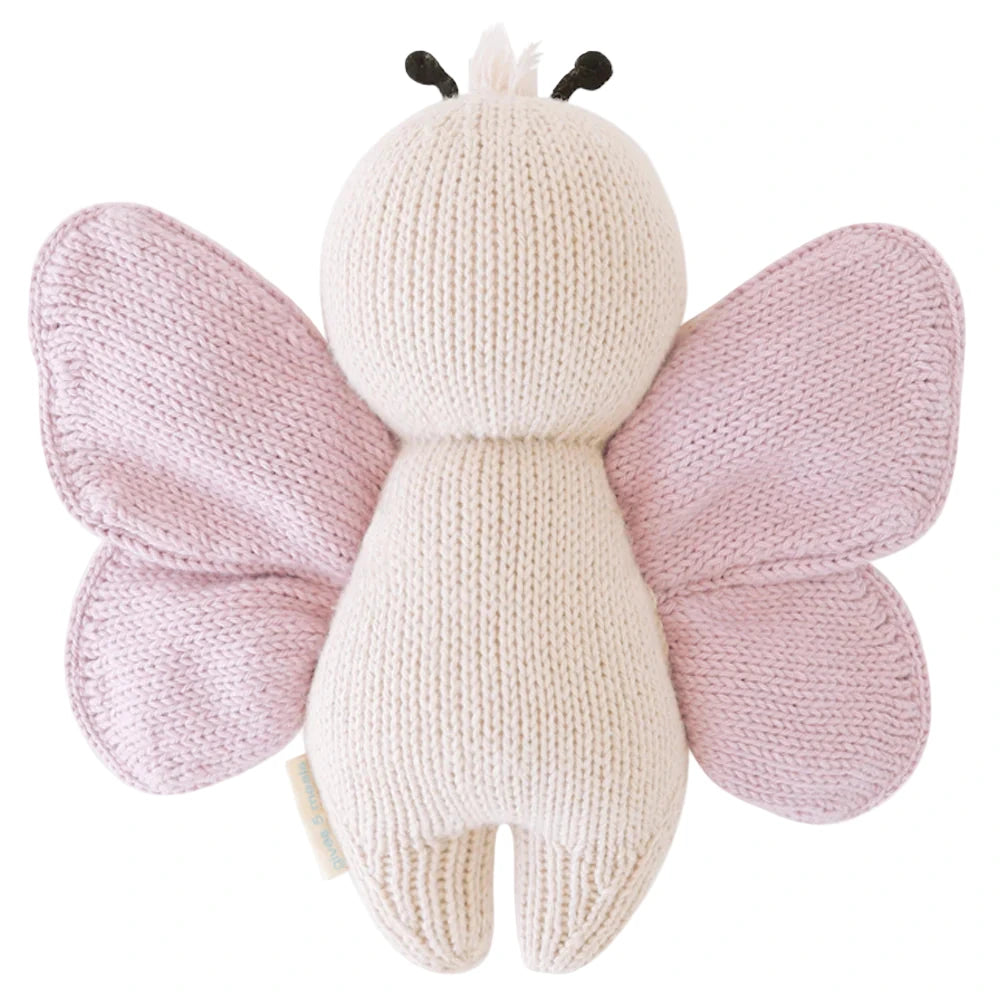 The Baby Butterfly by Cuddle + Kind is a hand-knit plush toy made from heirloom-quality Peruvian cotton yarn with a cream body and light pink wings, shown from the back.