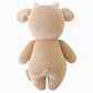 A rear view of the Baby Cow plush toy by Cuddle + Kind, handcrafted from natural cotton yarn in beige, featuring a small tail and horns, isolated against a white background.