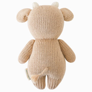 A rear view of the Baby Cow plush toy by Cuddle + Kind, handcrafted from natural cotton yarn in beige, featuring a small tail and horns, isolated against a white background.