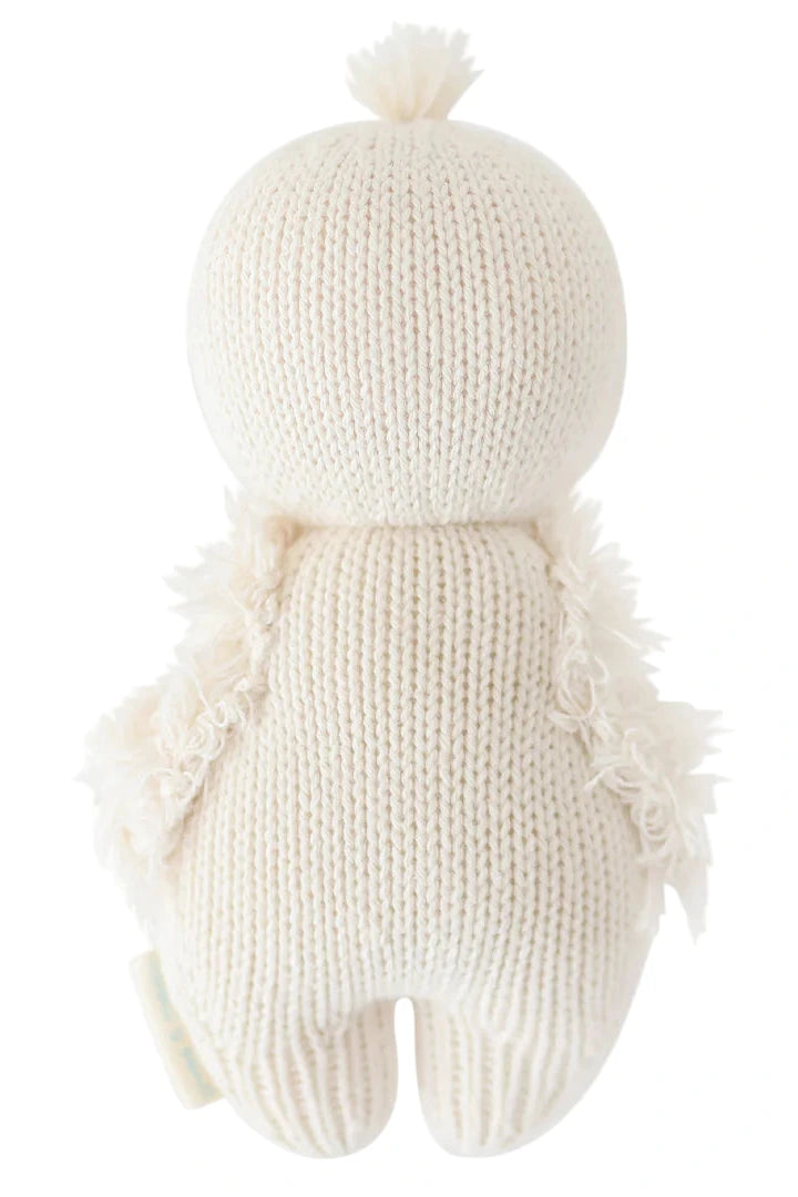 The Baby Gosling plush doll by Cuddle + Kind is hand-knit from Peruvian cotton yarn in a cream color, featuring textured arms, a round head, and a small tuft on top, and is shown facing away from the viewer.