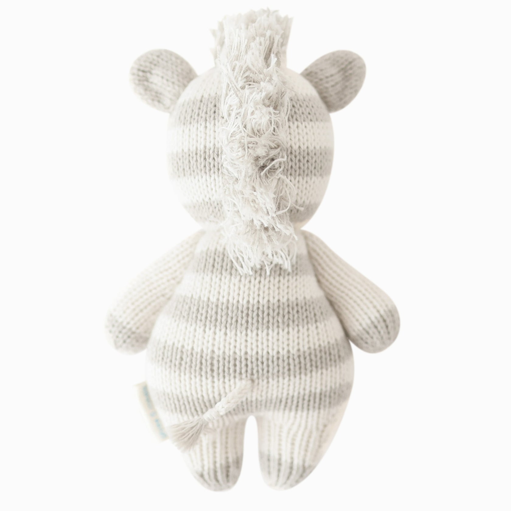 Introducing Cuddle + Kind's Zebra - Baby 7", a hand-knit plush zebra crafted from heirloom-quality Peruvian cotton yarn. This charming toy, seen from the back, features gray and white stripes, a short tail, and a shaggy mane—celebrating the artistry of hand-knit baby animals.