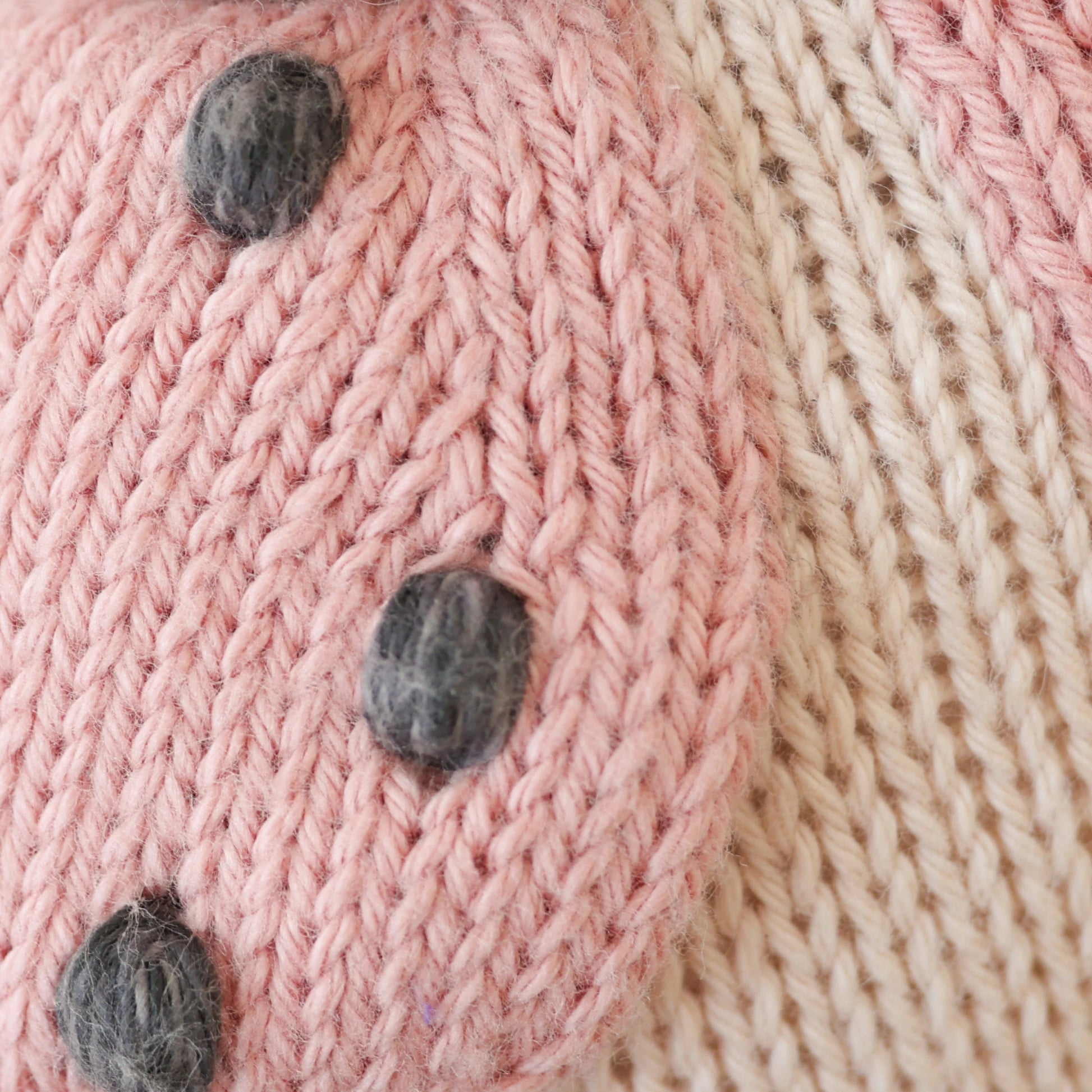 Close-up of Cuddle + Kind's Baby Ladybug: heirloom-quality pink and cream knit, featuring raised black dots—perfect for crafting hand-knit baby animals or collectible keepsakes.