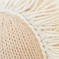 Close-up of handcrafted cotton yarn from the Baby Pony by Cuddle + Kind, featuring a knitted pattern on the left in beige and off-white woven fibers, with loose fringe threads on the right.