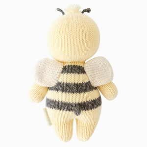 The Cuddle + Kind Bee - Baby 7" is an heirloom-quality, hand-knit plush bee doll, pictured from the back with yellow and black stripes, small wings, and two antennae—a charming addition to any collection of hand-knit baby animals.