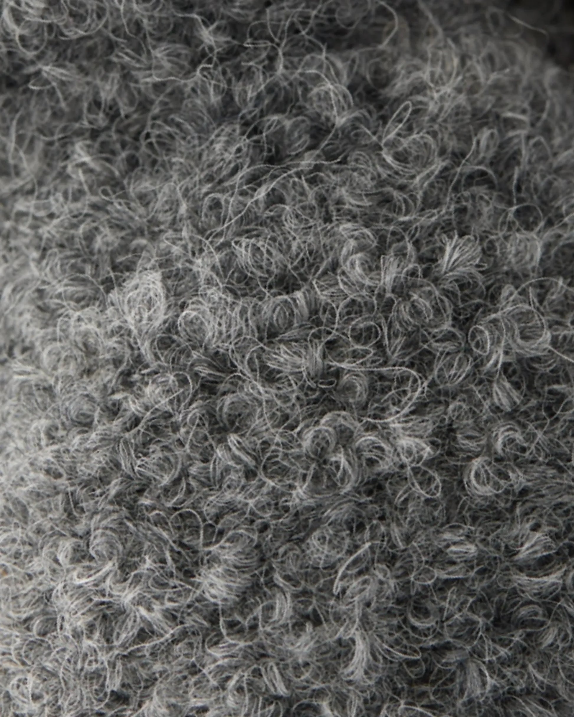 Close-up of a textured gray wool fabric with tight curls and loops, showing detailed fibers and a soft, fuzzy appearance—just like the gentle finish found on the Baby Bat - Charcoal by Cuddle + Kind.