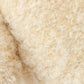 Close-up of light beige, curly wool fibers on the Baby Boucle Bear - Honey by Cuddle + Kind, highlighting the heirloom-quality texture and fine strands ideal for hand-knit baby animals.