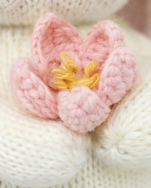 Close-up of Cuddle + Kind’s Baby Bunny - Blooming Tulip, featuring a pink and yellow crocheted flower handcrafted from heirloom-quality Peruvian cotton, displayed on a white knitted background.