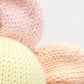 Close-up of three knitted fabrics in pastel colors—pink, yellow, and peach—arranged with the pink and peach pieces partially overlapping the yellow one. Each piece is crafted from soft, handcrafted cotton yarn by Cuddle + Kind, adding a gentle touch perfect for creating an heirloom Baby Daisy - Sunshower or a soft baby toy.