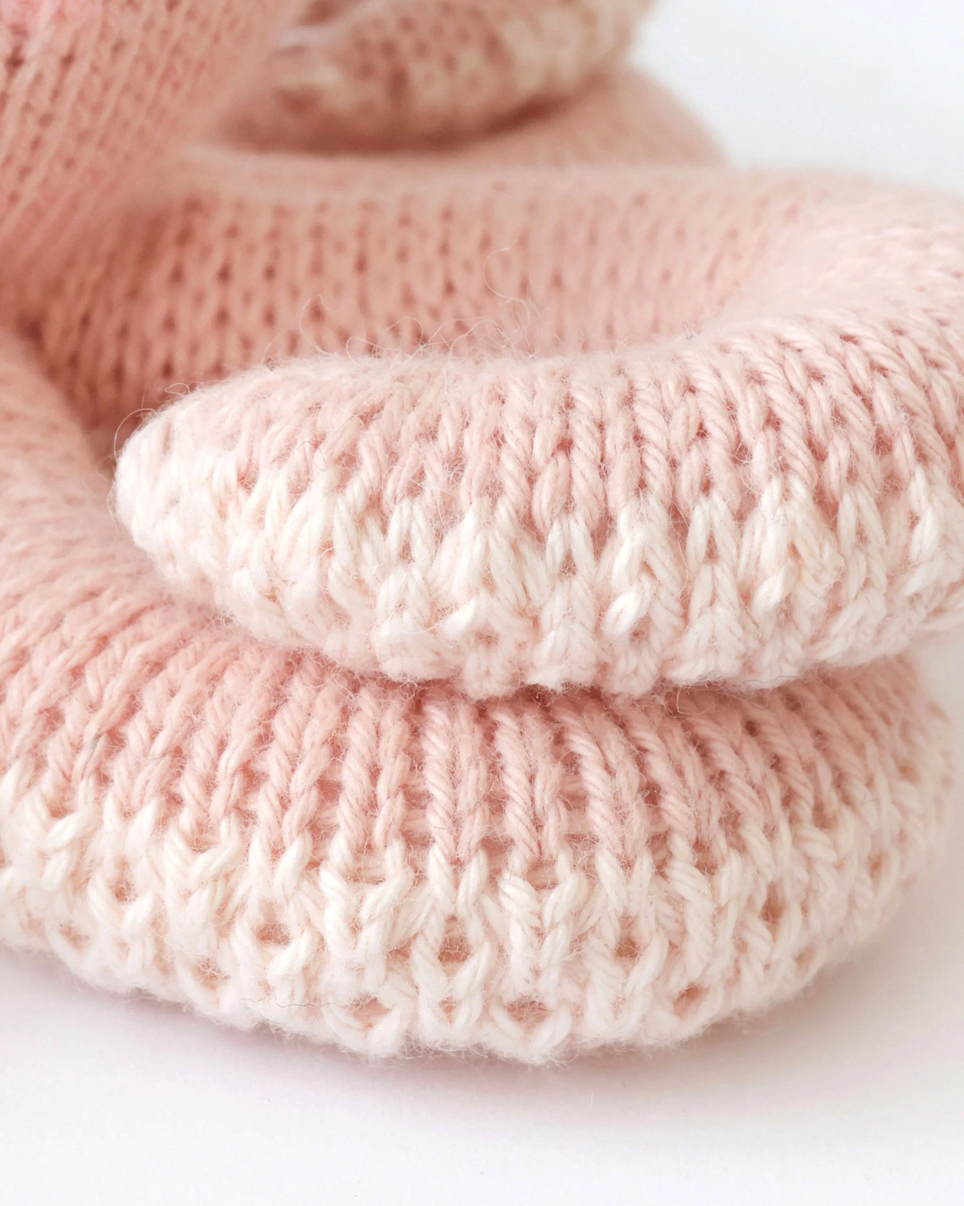 Close-up of two Baby Octopus - Soft Coral Pink booties by Cuddle + Kind, stacked together on a white background, lovingly crafted from premium Peruvian cotton yarn.