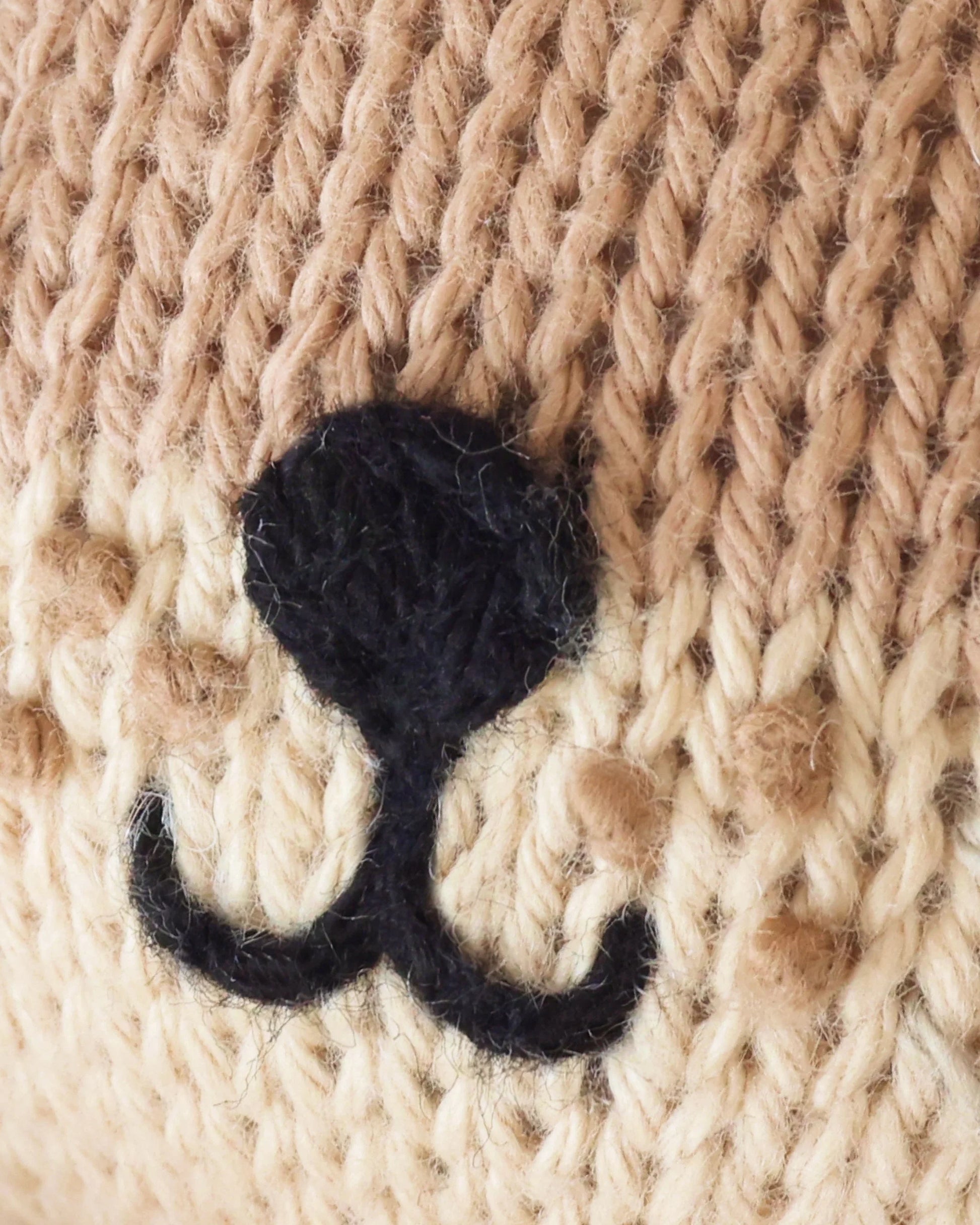 Close-up of beige knitted fabric handcrafted from Peruvian cotton, featuring a black, upside-down “Y” shaped stitched embroidery on the Baby Otter by Cuddle + Kind.