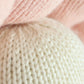 Close-up of two knitted fabrics, one in pale pink and the other in off-white, handcrafted from natural Peruvian cotton for the Baby Pearl by Cuddle + Kind, highlighting the detailed texture and stitching pattern of the yarn.