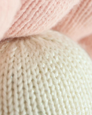 Close-up of two knitted fabrics, one in pale pink and the other in off-white, handcrafted from natural Peruvian cotton for the Baby Pearl by Cuddle + Kind, highlighting the detailed texture and stitching pattern of the yarn.