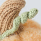Close-up of the Baby Pumpkin by Cuddle + Kind, a knitted object featuring a brown stem and green, twisted vine detail, lovingly handcrafted from soft cotton yarn—an ideal companion for your baby.
