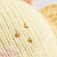 Close-up of the Cuddle + Kind Baby Sun, a knitted yellow fabric made from soft Peruvian cotton yarn, featuring three small gold embroidered dots with hints of pink and orange stitching in the background.