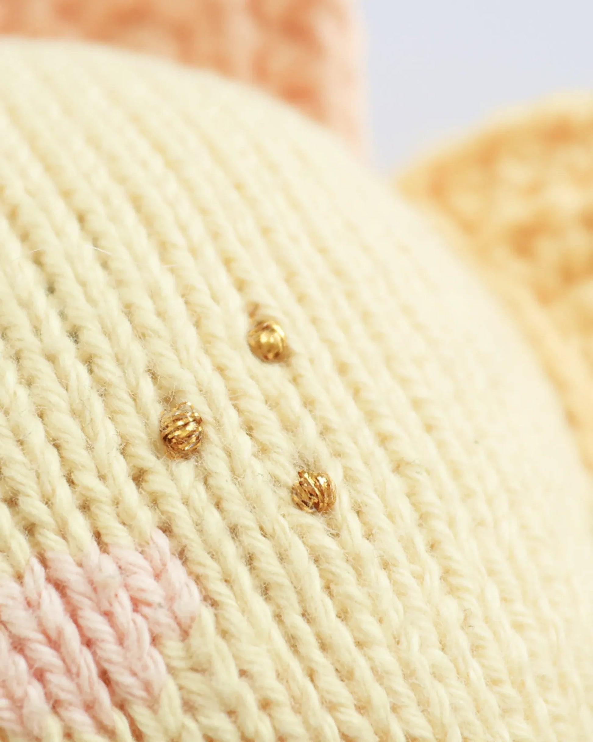 Close-up of the Cuddle + Kind Baby Sun, a knitted yellow fabric made from soft Peruvian cotton yarn, featuring three small gold embroidered dots with hints of pink and orange stitching in the background.