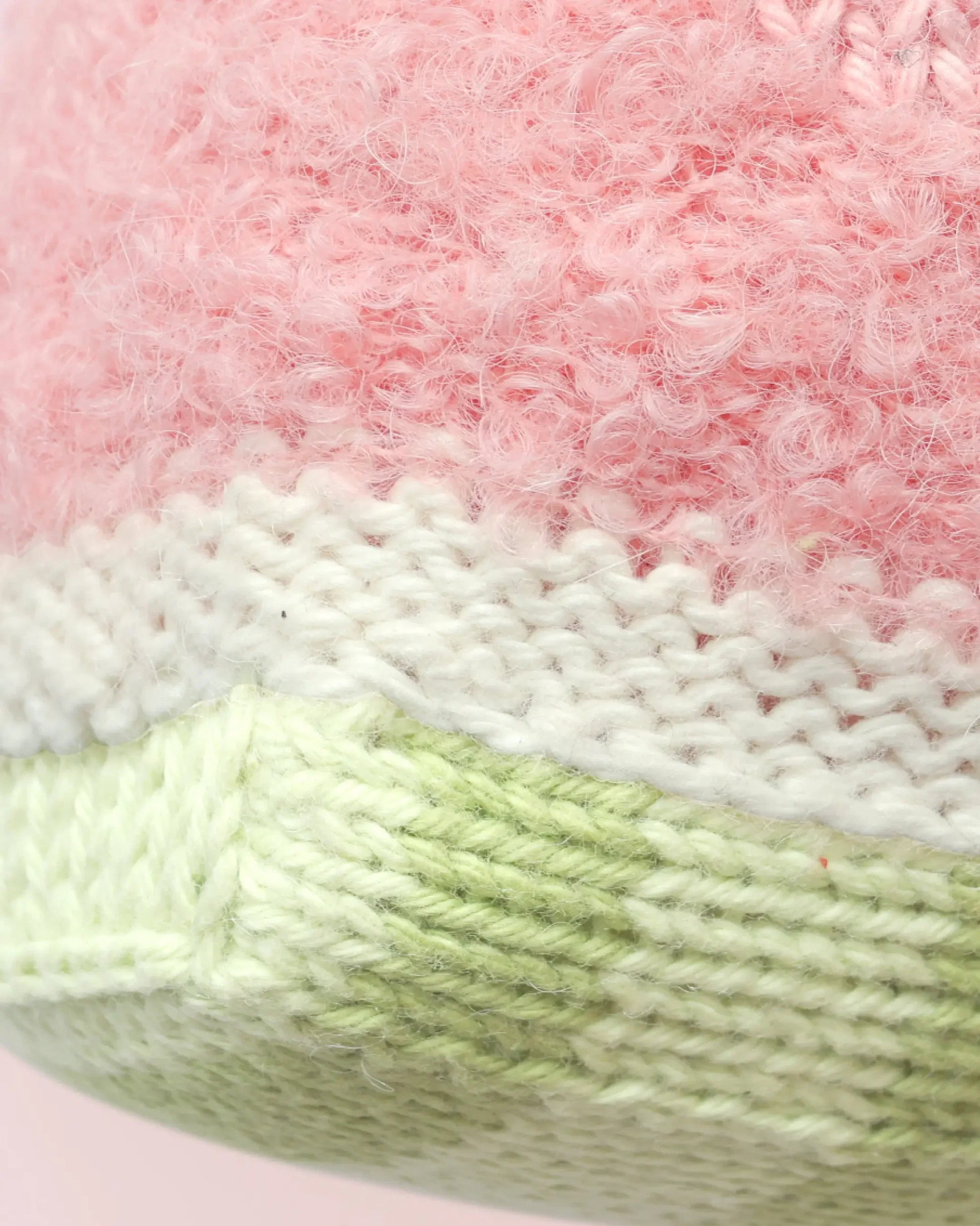 Close-up of the Baby Watermelon knitted fabric by Cuddle + Kind, featuring pink, white, and light green yarn with textured stitches and soft material—perfect for creating a handcrafted cotton toy or cherished soft baby companion.