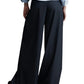 A person in a light blue shirt and TWP New Didi Wool Pants from TWP, featuring elegant wide-leg pleats, is standing against a white background.