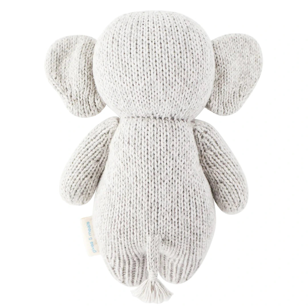 The Baby Elephant plush toy by Cuddle + Kind features large ears, short limbs, and a small tail. Hand-knit from heirloom-quality Peruvian cotton yarn in gray, it’s perfect for baby animal fans. Shown from the back.