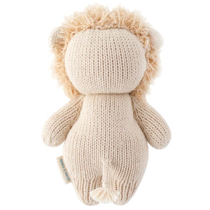 The Baby Lion by Cuddle + Kind is an heirloom-quality knitted stuffed toy shown from the back, highlighting its soft beige yarn texture, fluffy mane, and small tail.