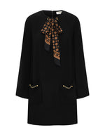 Zimmermann Utility Tunic Dress in black, featuring long sleeves, a patterned neck tie, and two front pockets accented with gold-tone chains.