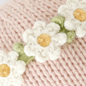 Close-up of the Baby Bunny - Rose w/ Ivory Floral by Cuddle + Kind, featuring pink handcrafted cotton knit fabric accented with white and yellow crochet daisy flowers and green leaves.