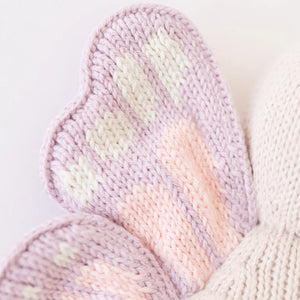 Close-up of the Cuddle + Kind Baby Butterfly: a soft toy adorned with hand-knit pastel butterfly wings in light purple, pink, and white, made from heirloom-quality Peruvian cotton yarn.