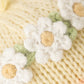 Close-up of Cuddle + Kind’s Baby Duckling Ivory Floral: handcrafted white flowers with yellow centers and green leaves on soft, light yellow knit, adding heirloom charm.